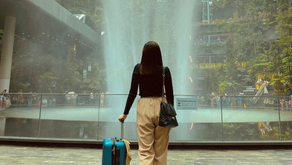 devojka sa koferom ispred fontane na aerodromu