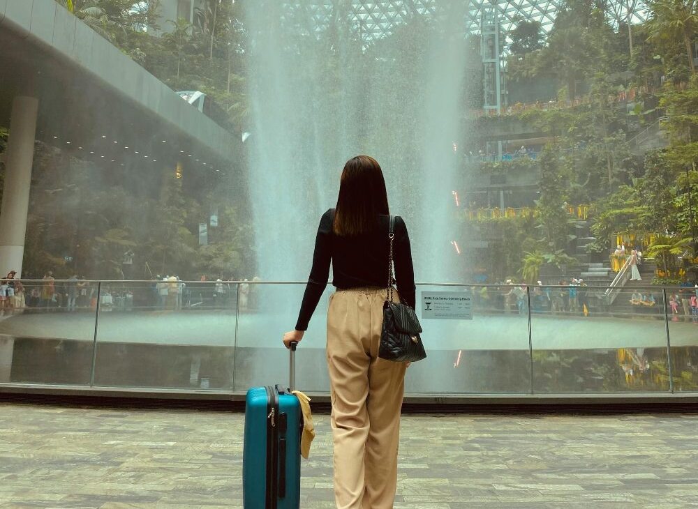 devojka sa koferom ispred fontane na aerodromu