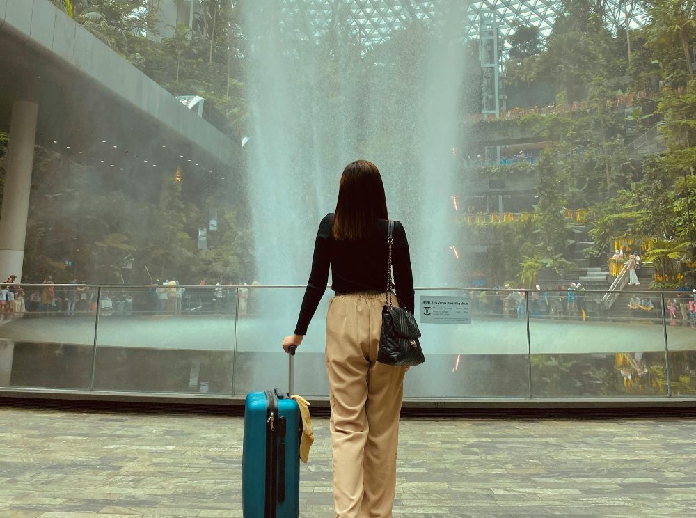 devojka sa koferom ispred fontane na aerodromu